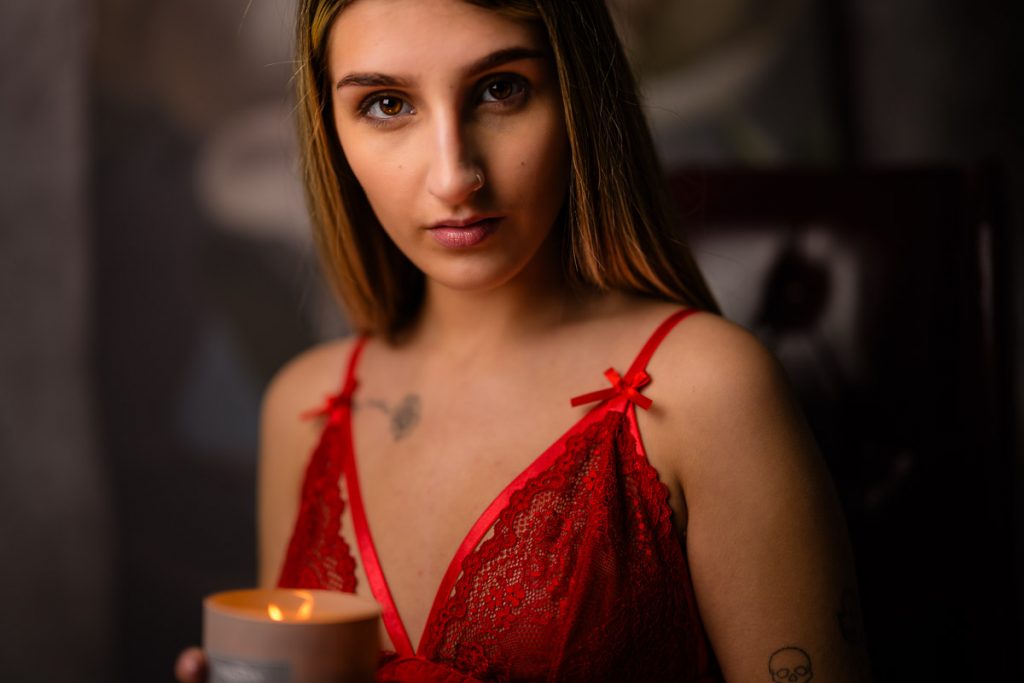 Blond model wearing red baby doll, holding a lit candle.  The light is low and there is a red glow in her eyes.