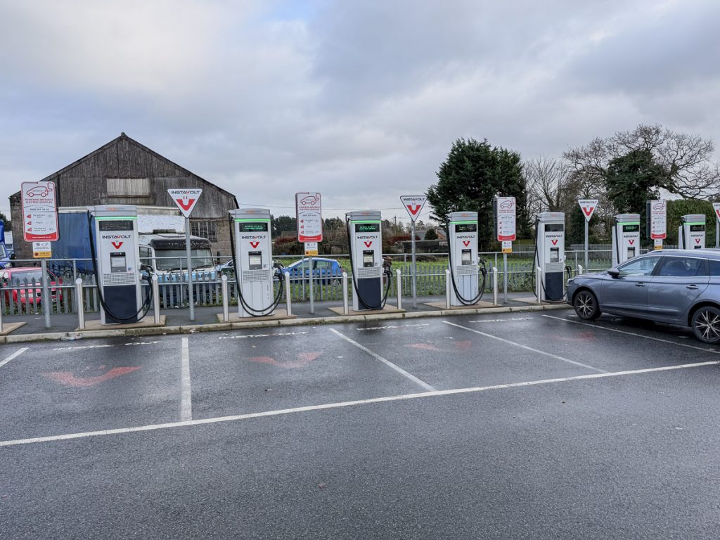 A row of electrical car chargers for EV's.  One car a grey MG estate (Station wagon)