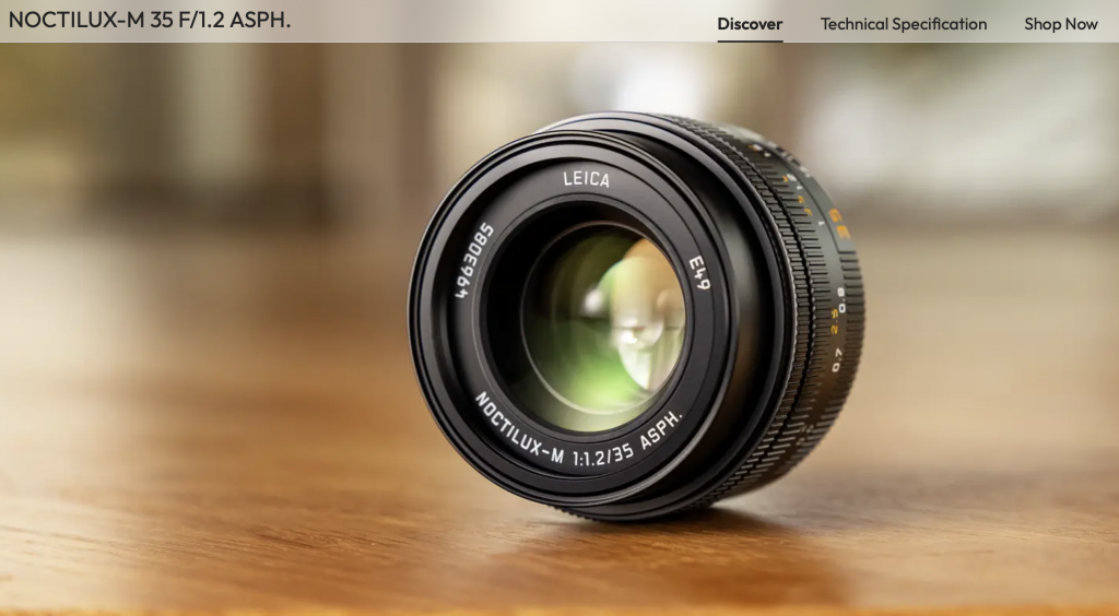 A advertising picture of the new Leica Noctilux 35mm lens.  The lens is sat on a wooden desk and the lens glass can be seen.