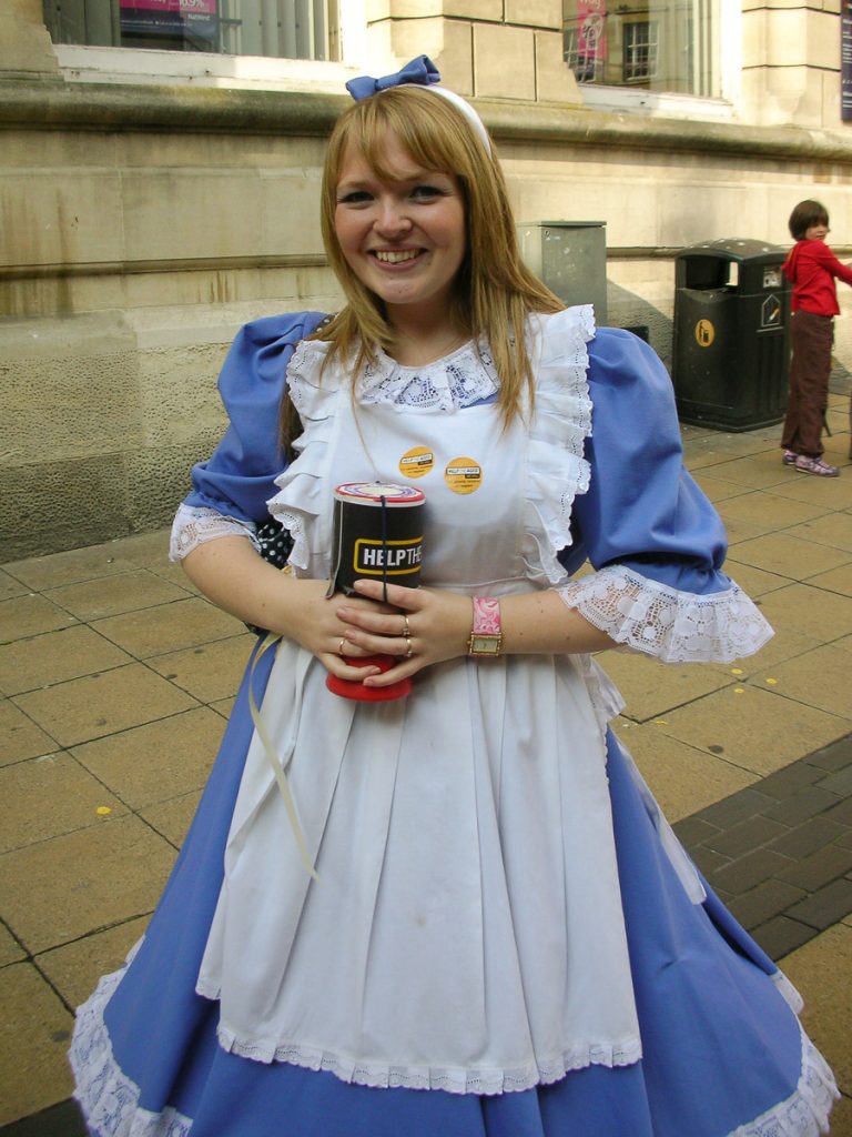 A young woman with a collection box on Lincoln high street.  She is dressed as Alice in Wonderland.