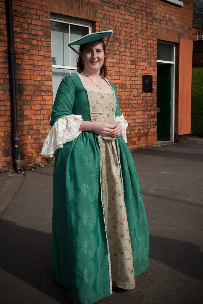 A young woman in a early period dress posing on the street.