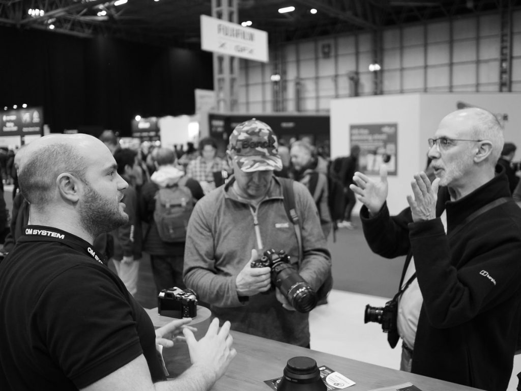 Black and White photo of a man talking to an Olympus representative. 