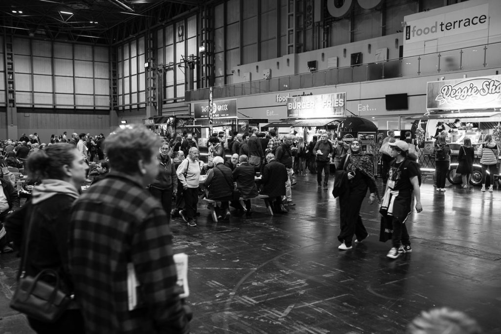 Food tables in front of the food stalls.  Very busy with lots of people around.