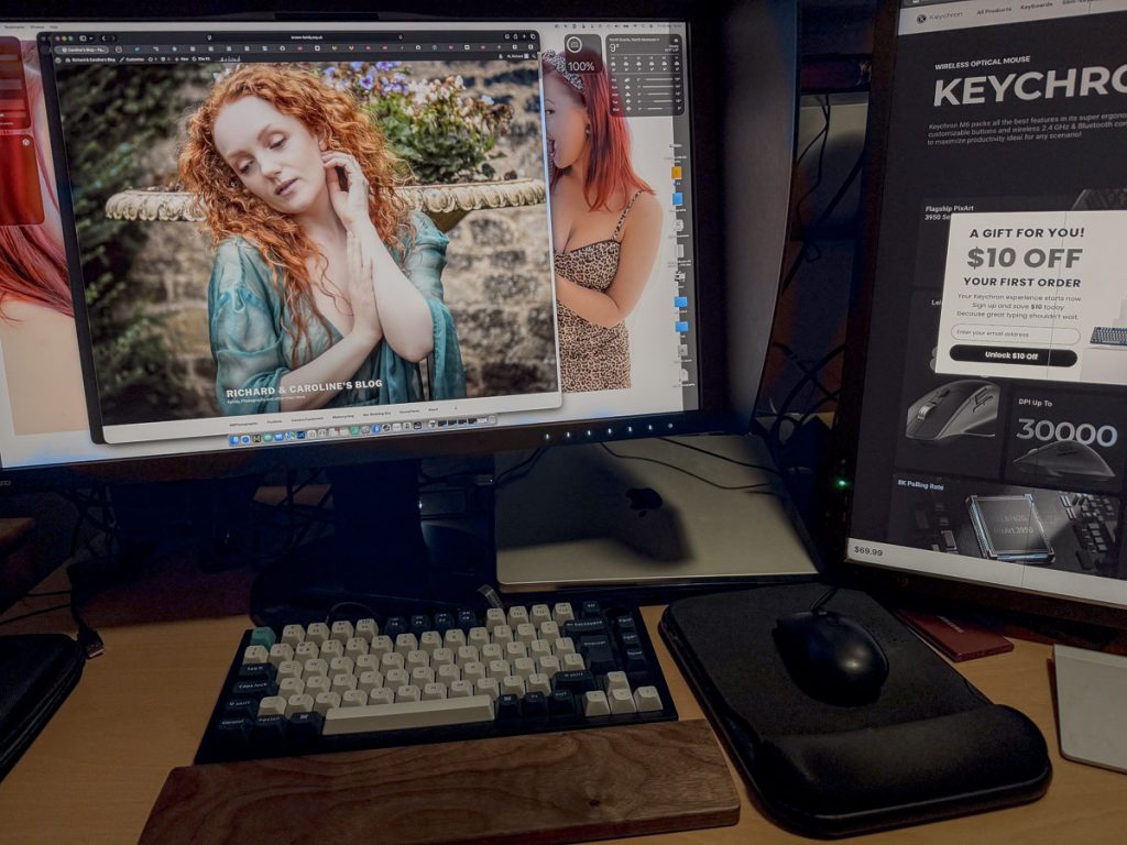 Photo of a crowded desk. Two monitors, a mechanical keyboard, mouse and trackpad can be seen.