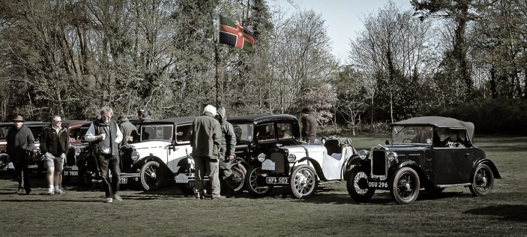 A large format film photograph of a line up of very old classic cars in a field.  The flag of the county of Lincolnshire can be seen flying.