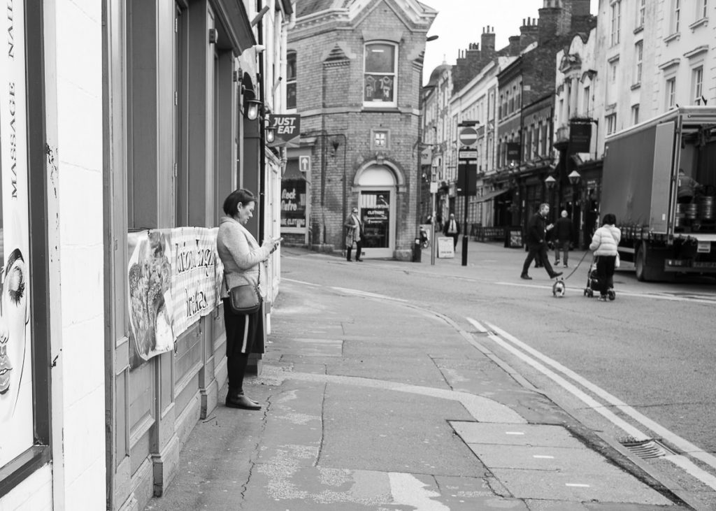 Street in Lincoln, with a woman leaning against a wall looking at her phone.