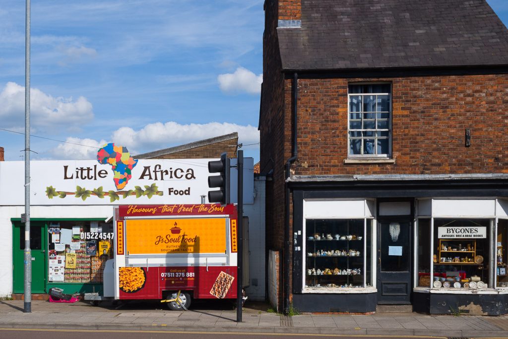 An African food shop next to an old antique shop. The bright colours of the food shop contrast with the dark tones of the old antique shop.