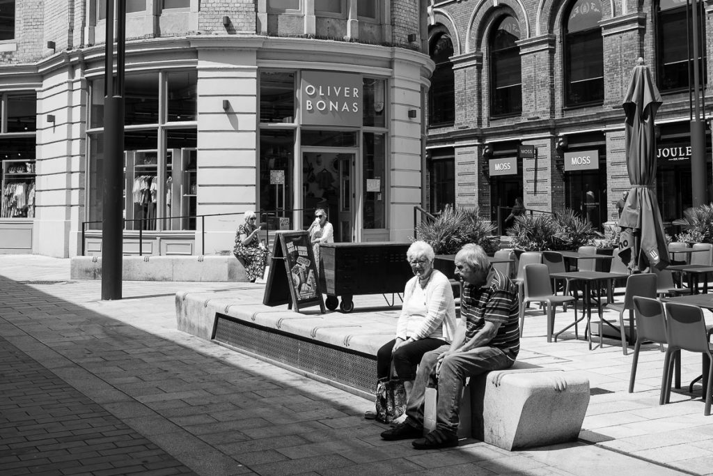 An older couple sat in the corn hill square in Lincoln. Both are sat resting after doing some shopping.