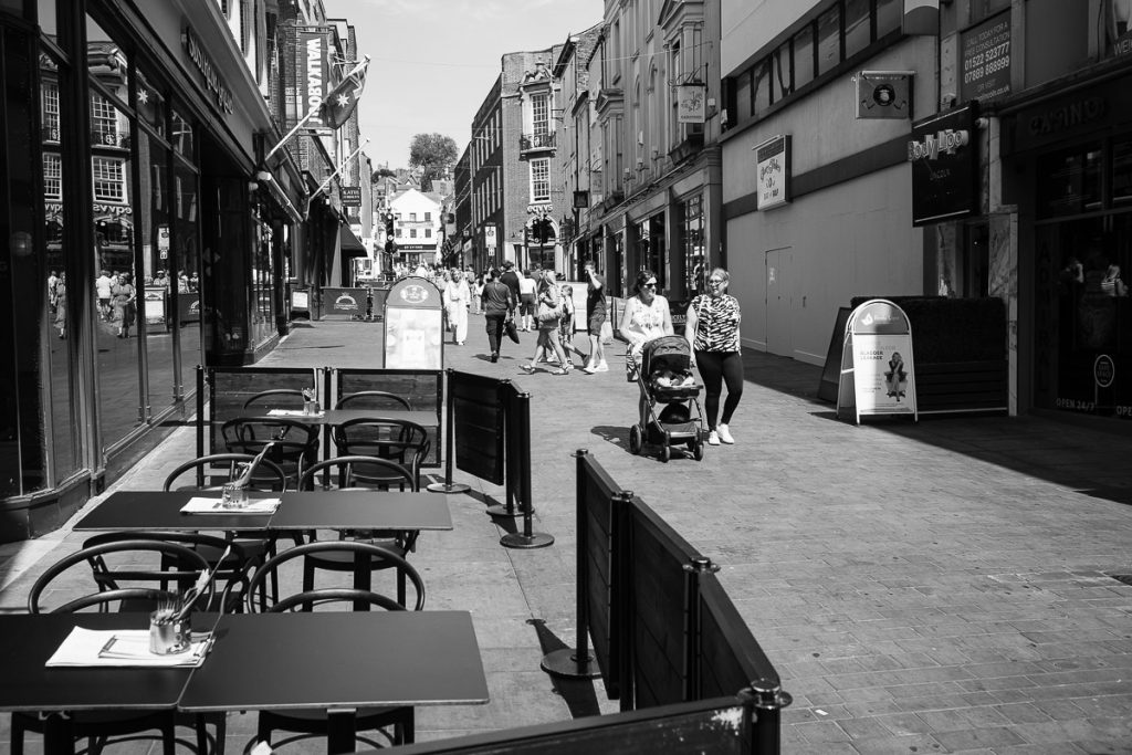 A view of Lincoln high street towards steep hill. It will soon be lunch so the tables are now out at the bars and coffee shops.