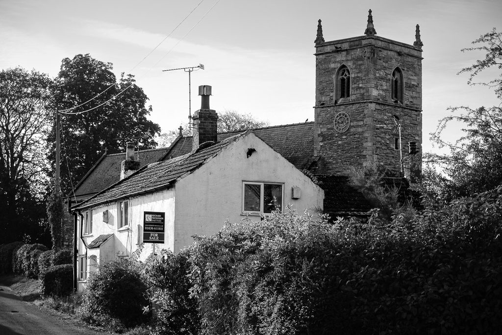 A white village cottage for sale and behind can be seen the old norman village church