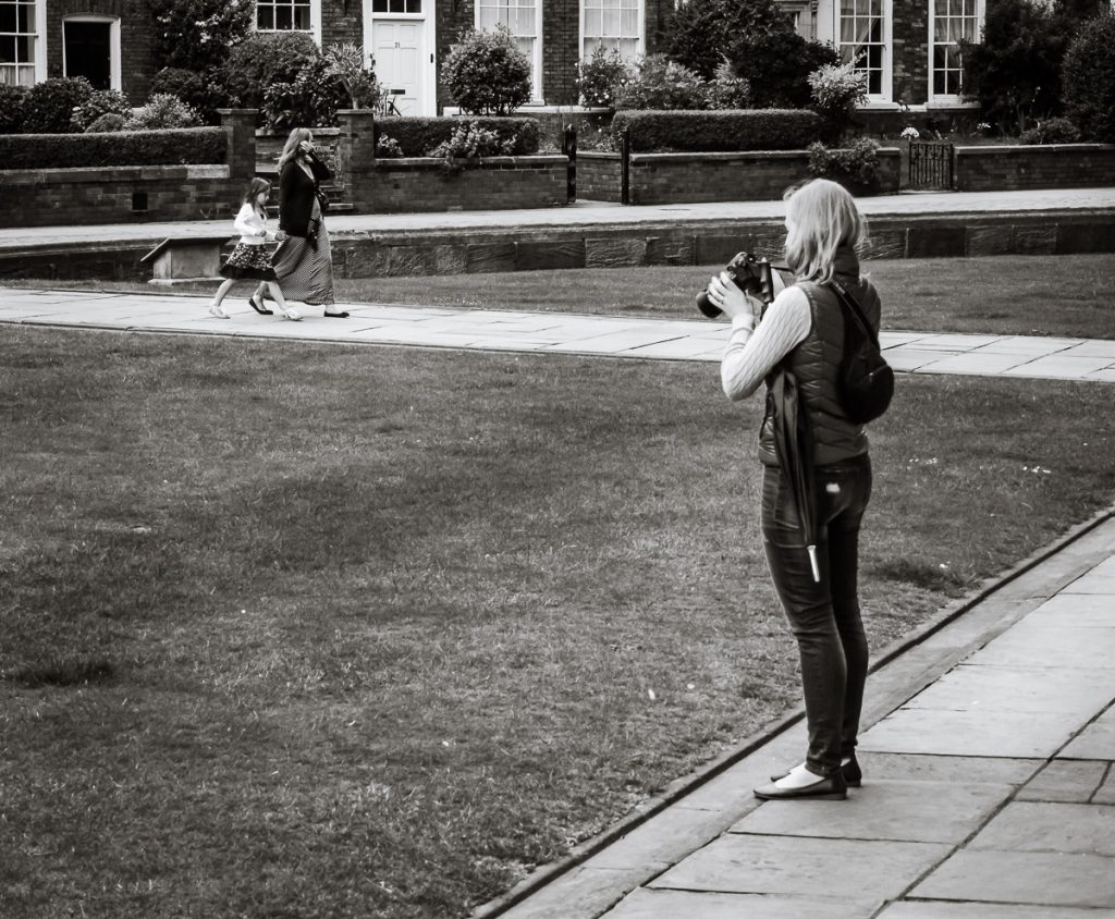 Young woman holding a large SLR, looking at the back. She is stood with Lincoln Cathedral behind her out of shot.