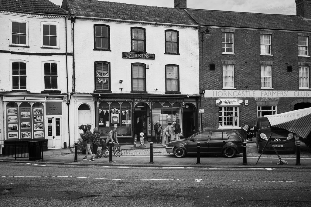 Centre of Horncastle, and some of the old buildings, Perkins shop and the Horncastle Farmers Club are the two main buildings in the picture. Some people walking and pushing a cycle can be seen.