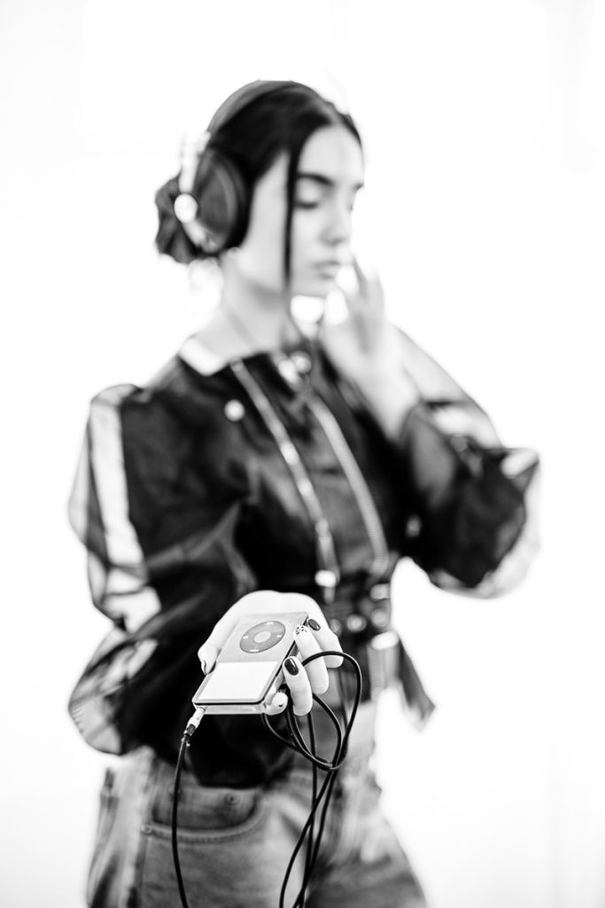 Model in leather jacket, wearing classic99 headphones and holding a classic Apple iPod
